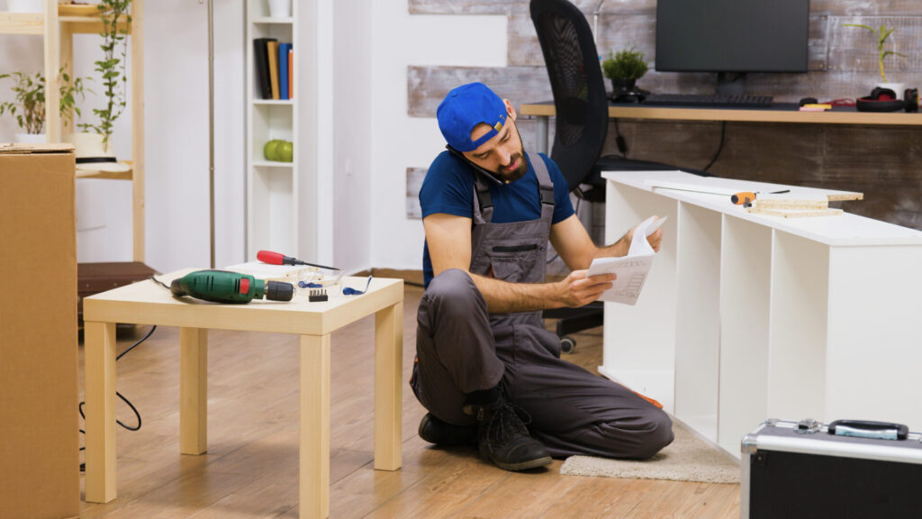 trabajador sexo masculino hablando telefono mientras ensambla muebles blancos casa nueva taladro electrico